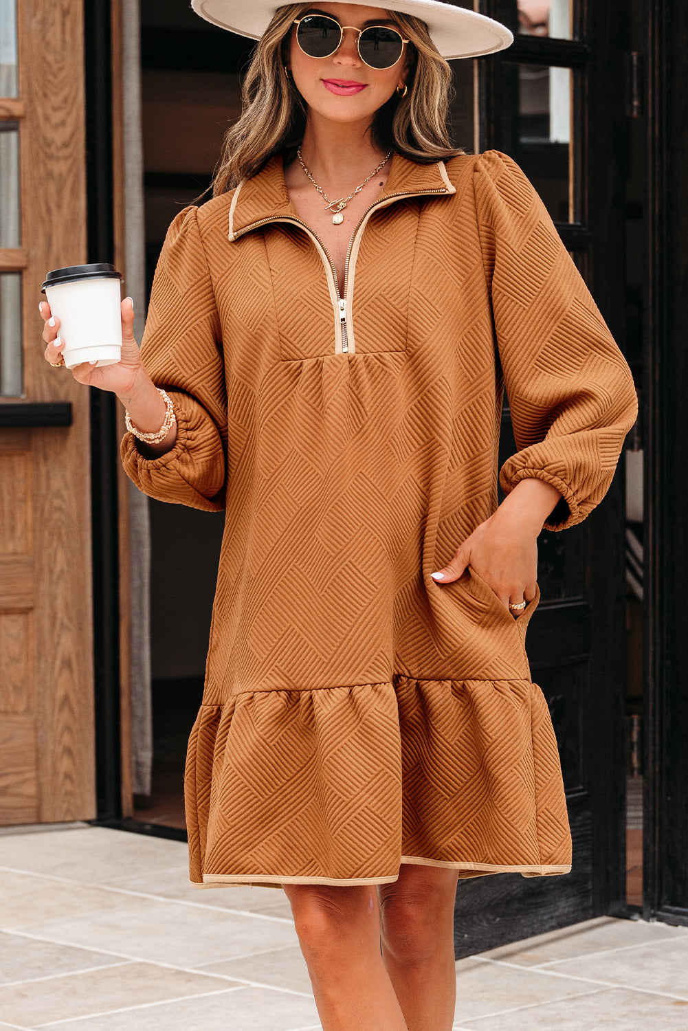 Woman in tan textured long sleeve mini dress with zipper detail, wearing hat and sunglasses