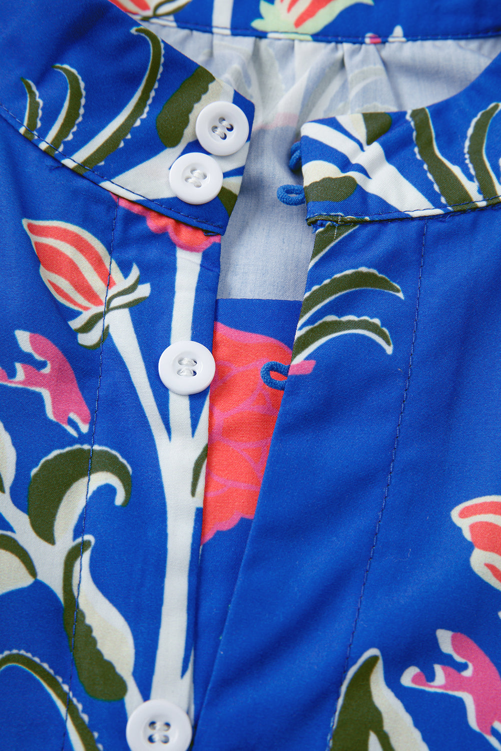 Close-up of blue floral shirt with white buttons and colorful tropical pattern.