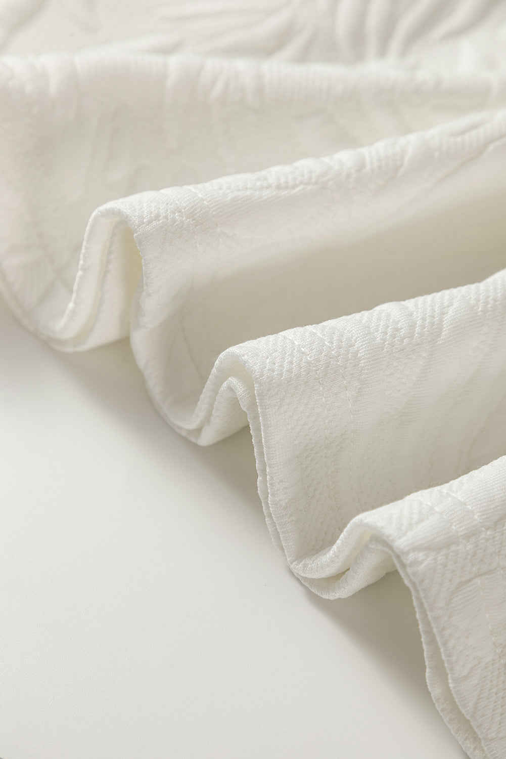 Close-up of soft white textured fabric with gentle folds on a light surface