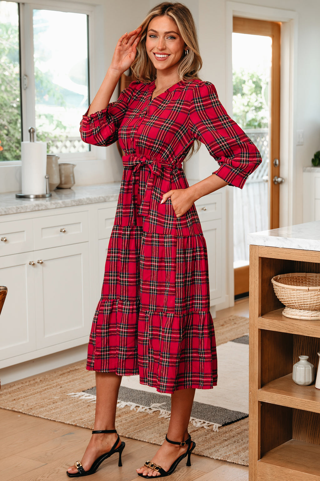 Woman wearing red plaid midi dress with tie waist and black sandals in modern kitchen