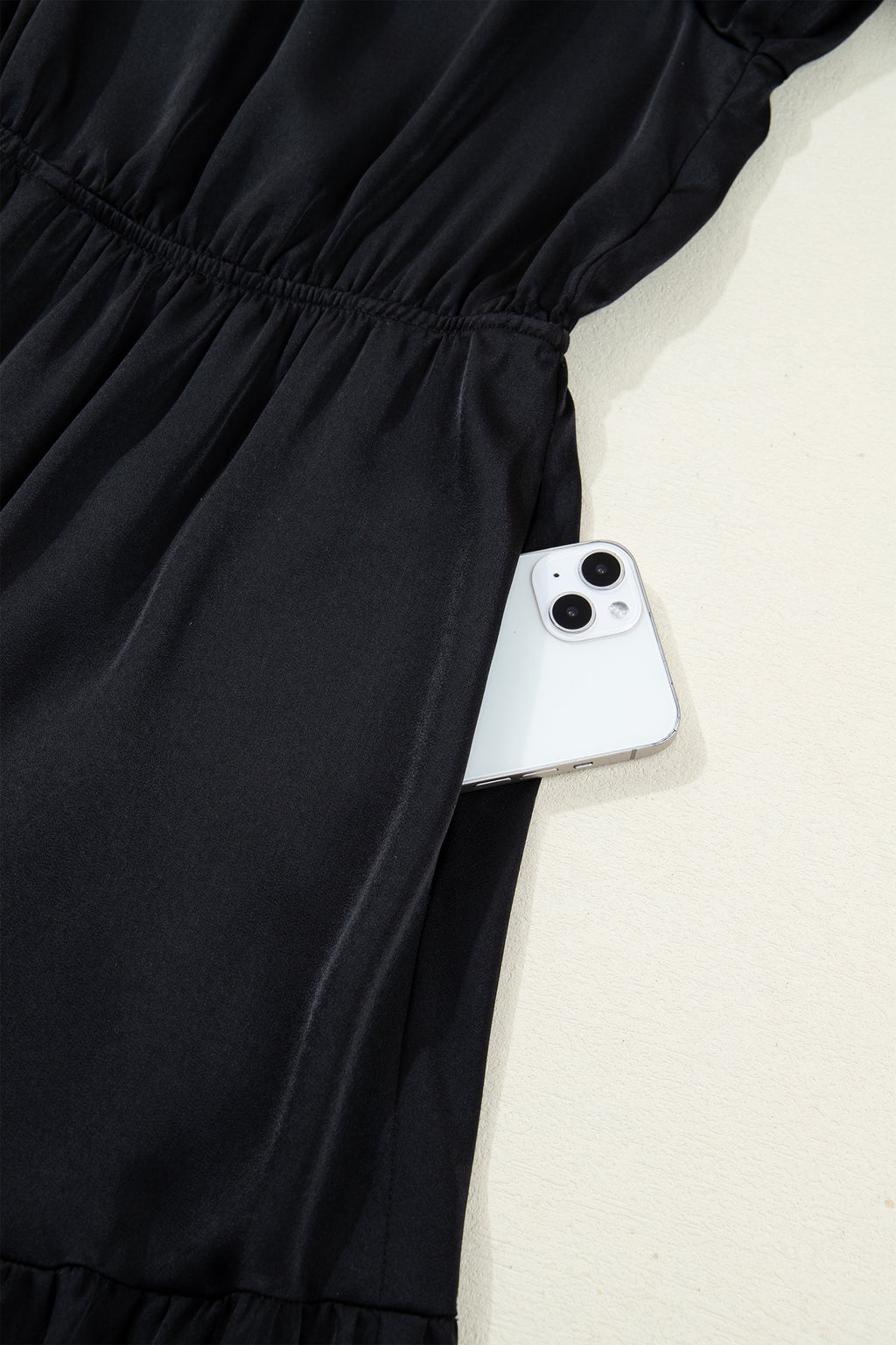 Black dress with side pocket holding a white smartphone on light background