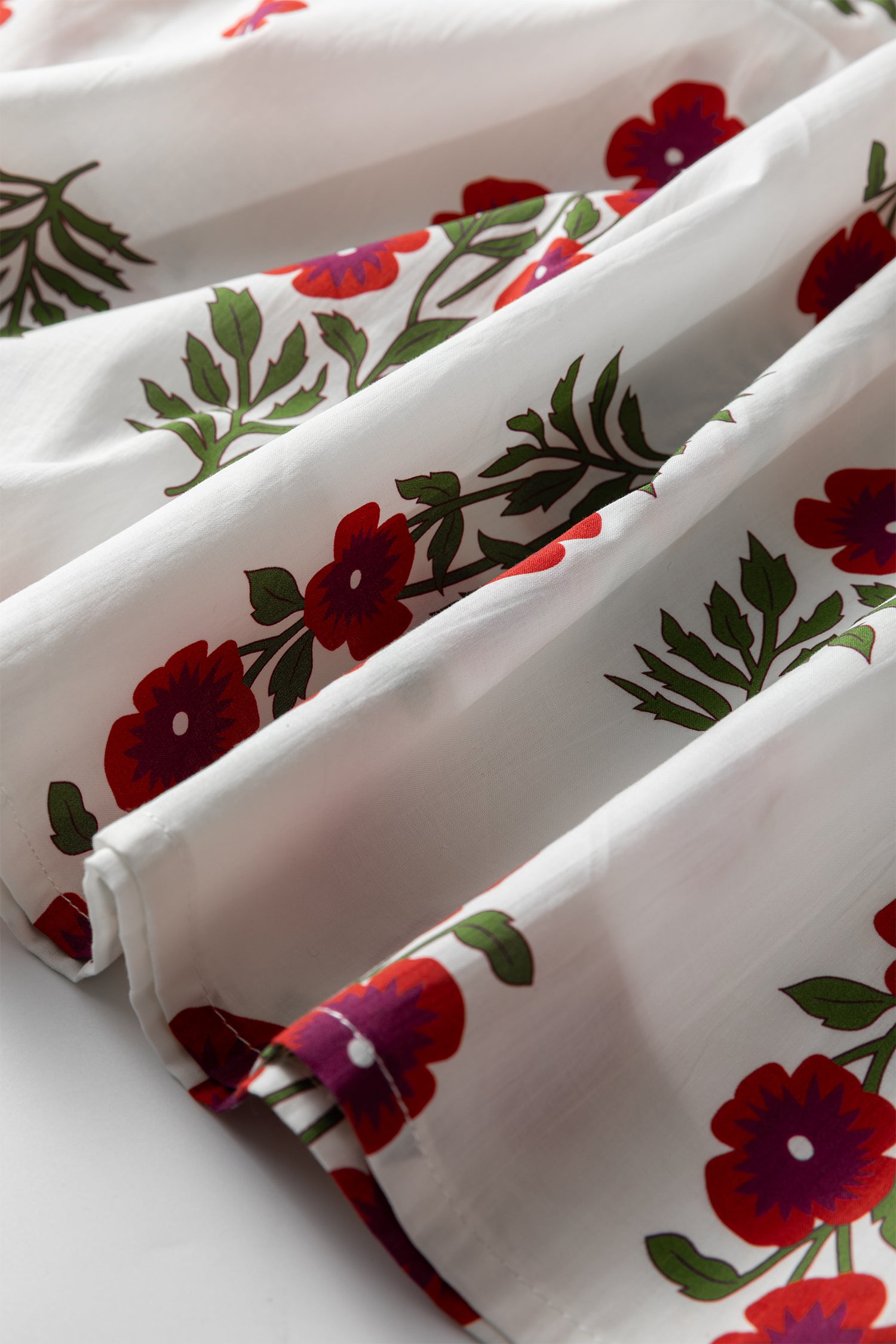White fabric with red floral pattern and green leaves, close-up textile detail