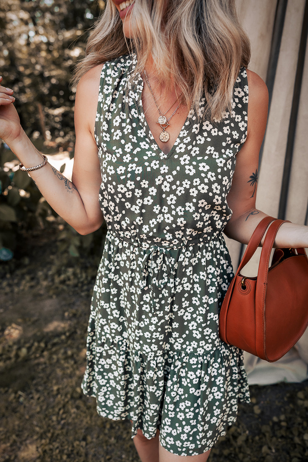 Woman wearing green floral summer dress, holding brown handbag outdoors