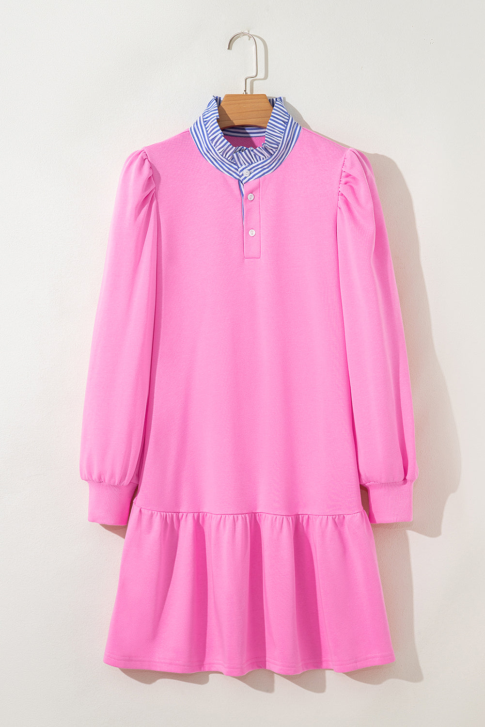 Pink long sleeve dress with ruffled hem and blue striped collar, hanging on wall