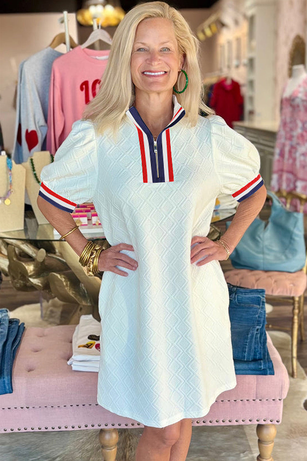Woman wearing a white textured short sleeve dress with red and navy striped collar, boutique setting
