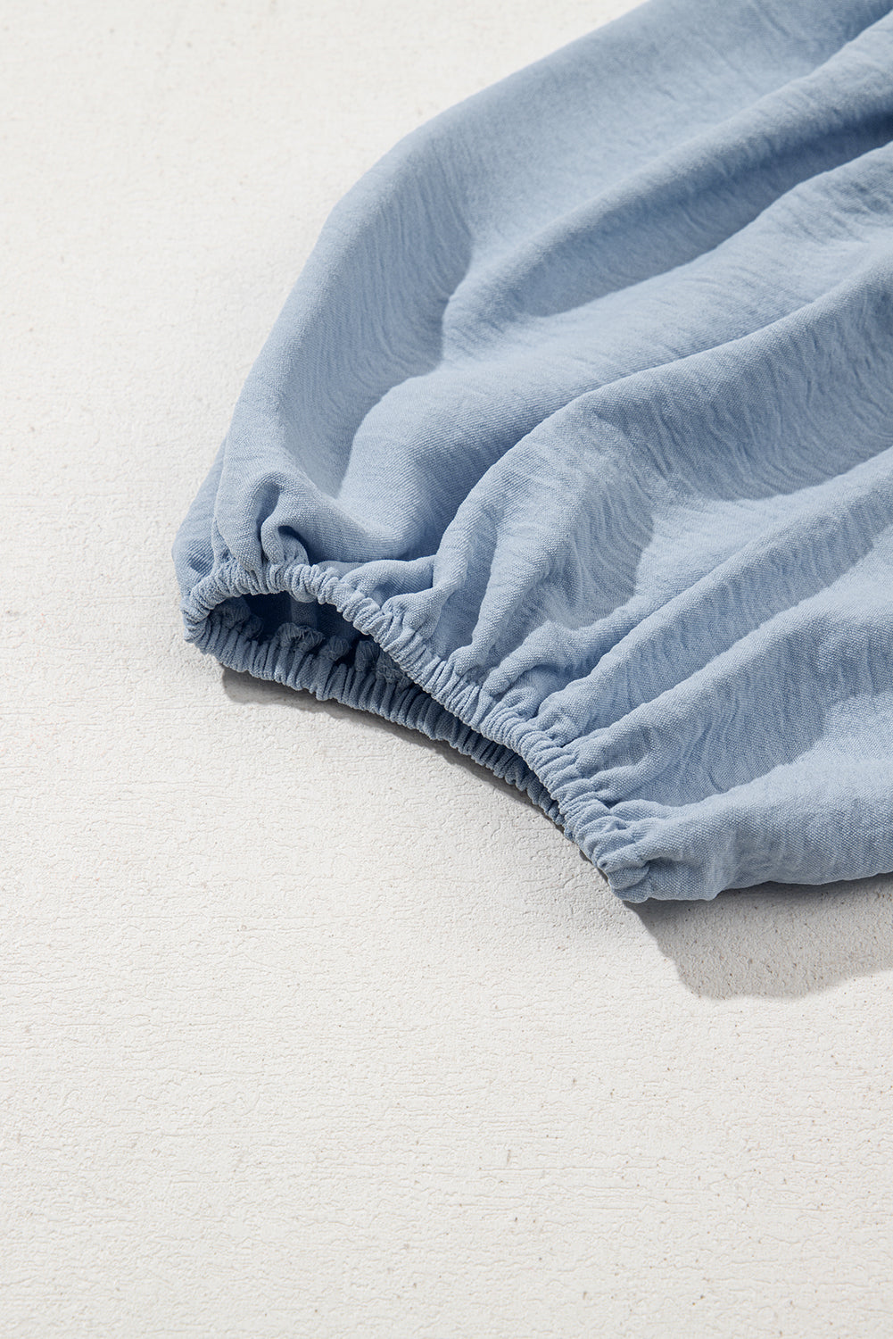 Close-up of light blue long sleeve with ruched elastic cuff on textured background