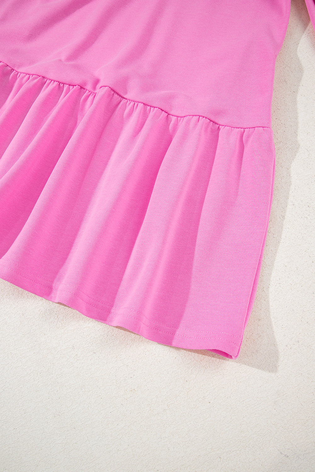 Close-up of pink ruffled hem dress on light textured background