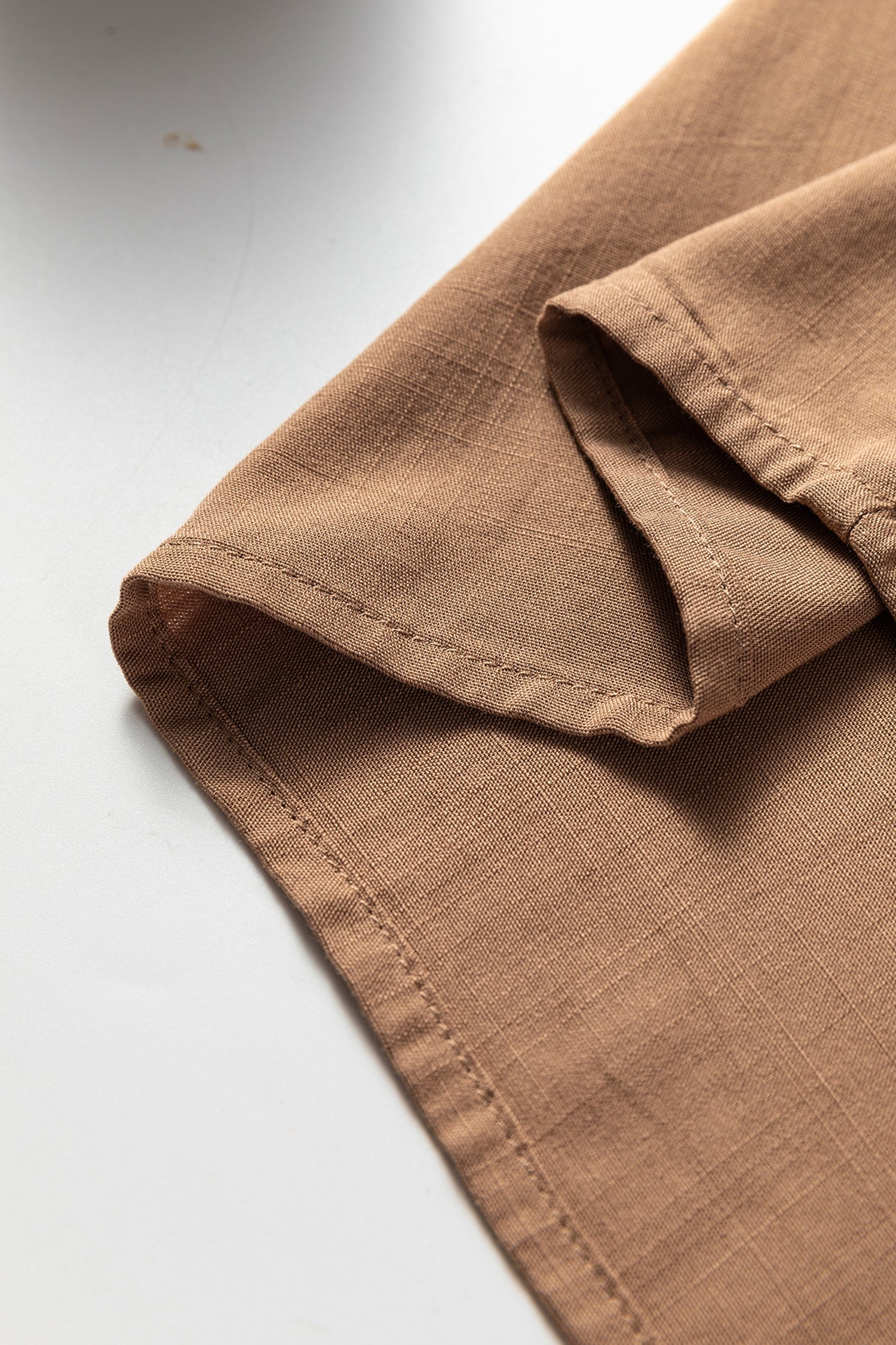 Close-up of brown linen shirt sleeve with visible stitching on white background