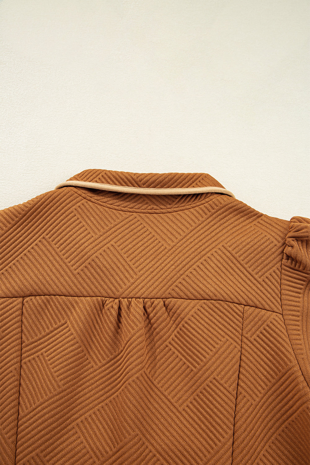 Closeup of brown textured fabric jacket with geometric pattern and piped collar