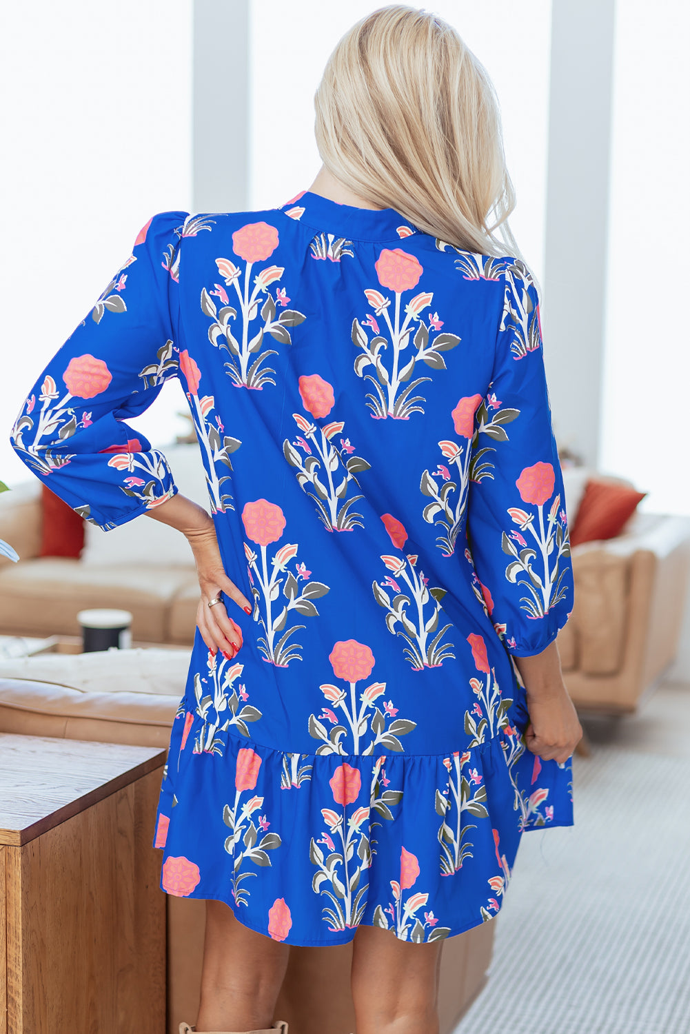 Woman wearing a blue floral print dress with pink flowers, shown from the back in a modern living room