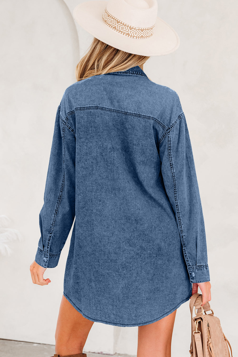 Woman in long sleeve denim shirt dress and beige hat holding tan handbag
