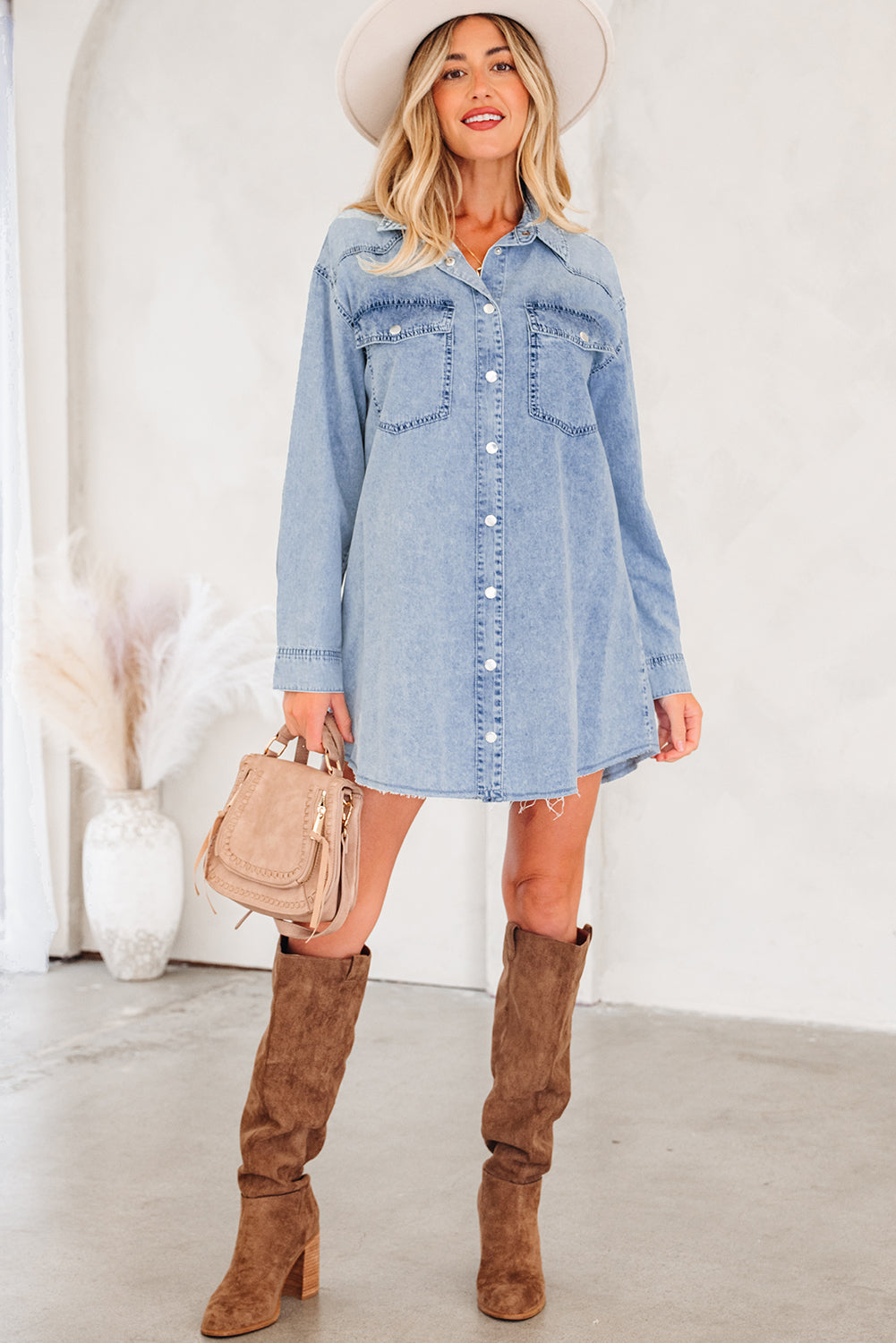 Woman in light blue denim shirt dress with brown suede knee boots, holding a beige handbag.