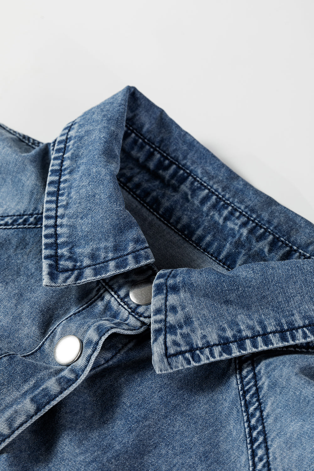 Close-up of blue denim shirt collar with metal snap buttons on white background