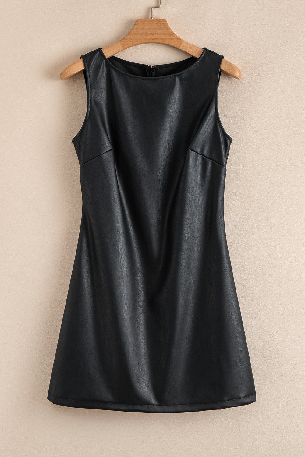 Sleeveless black faux leather mini dress on a wooden hanger against a beige wall
