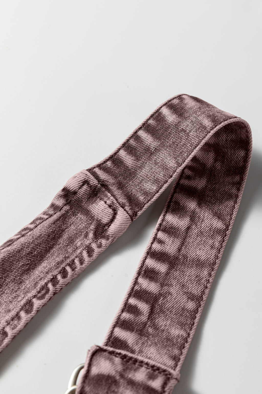 Close-up of a mauve textured fabric belt with stitching detail on a white background