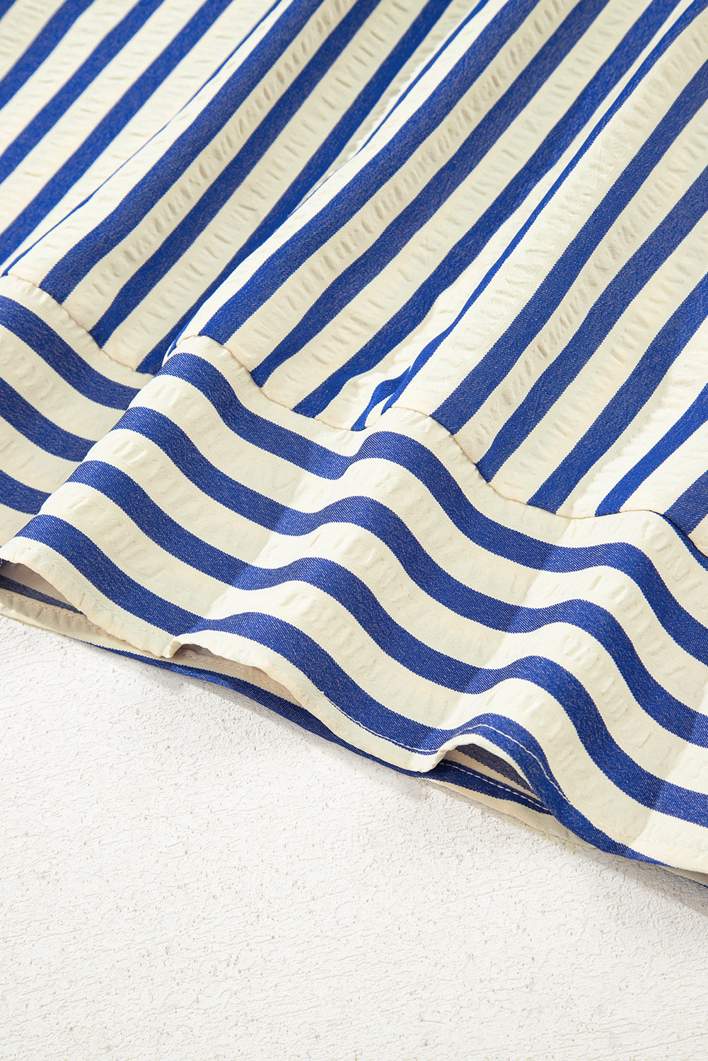 Blue and white striped fabric close-up, textured cotton material, wavy hem detail