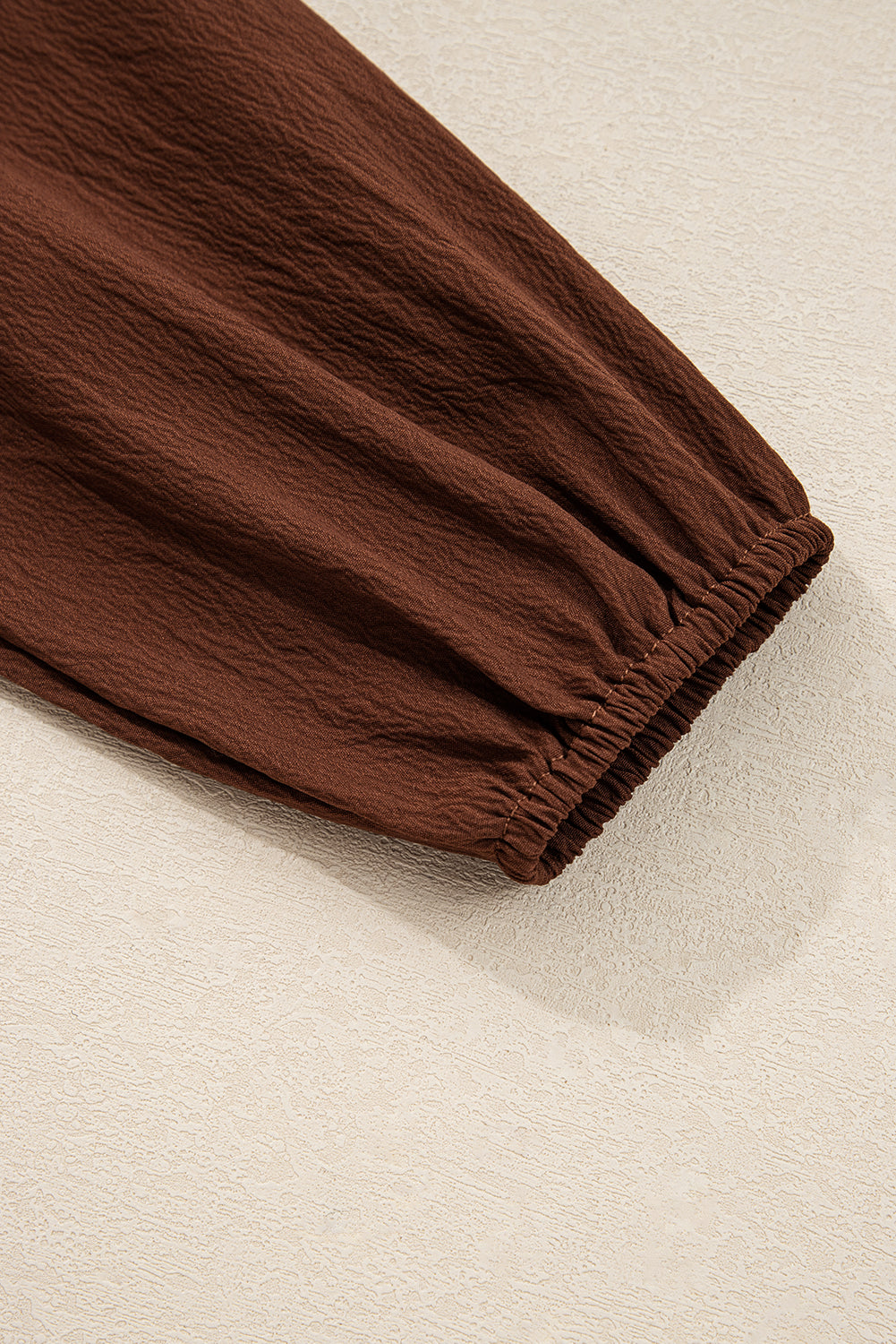Close-up of a brown textured long sleeve with an elastic cuff on a neutral background
