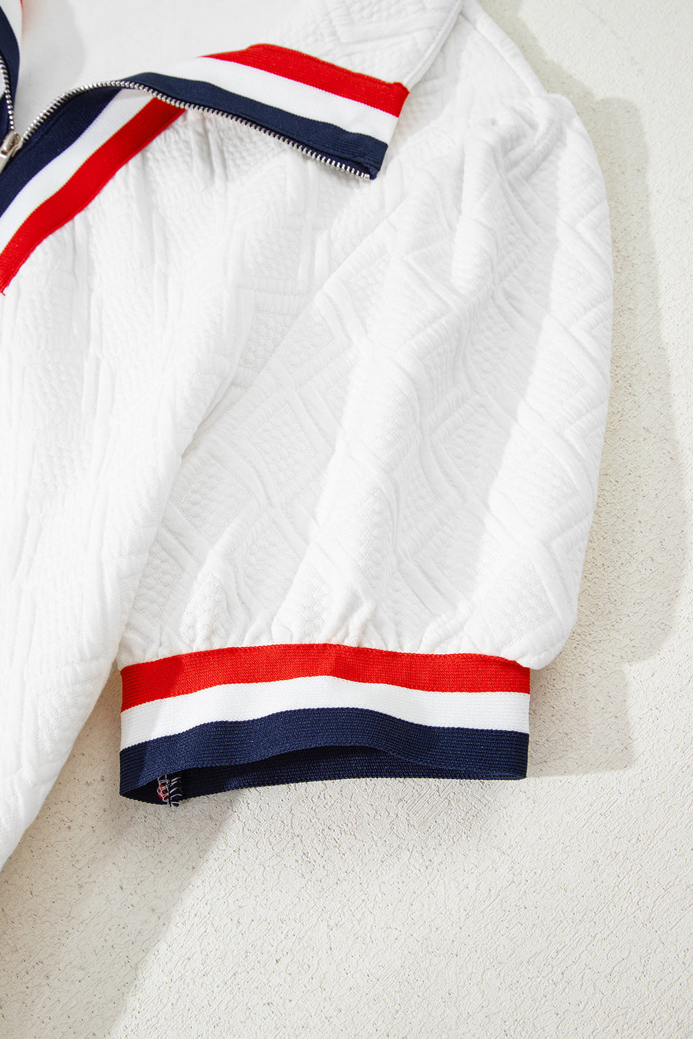 White textured jacket sleeve with red, white, and blue striped trim and zipper detail