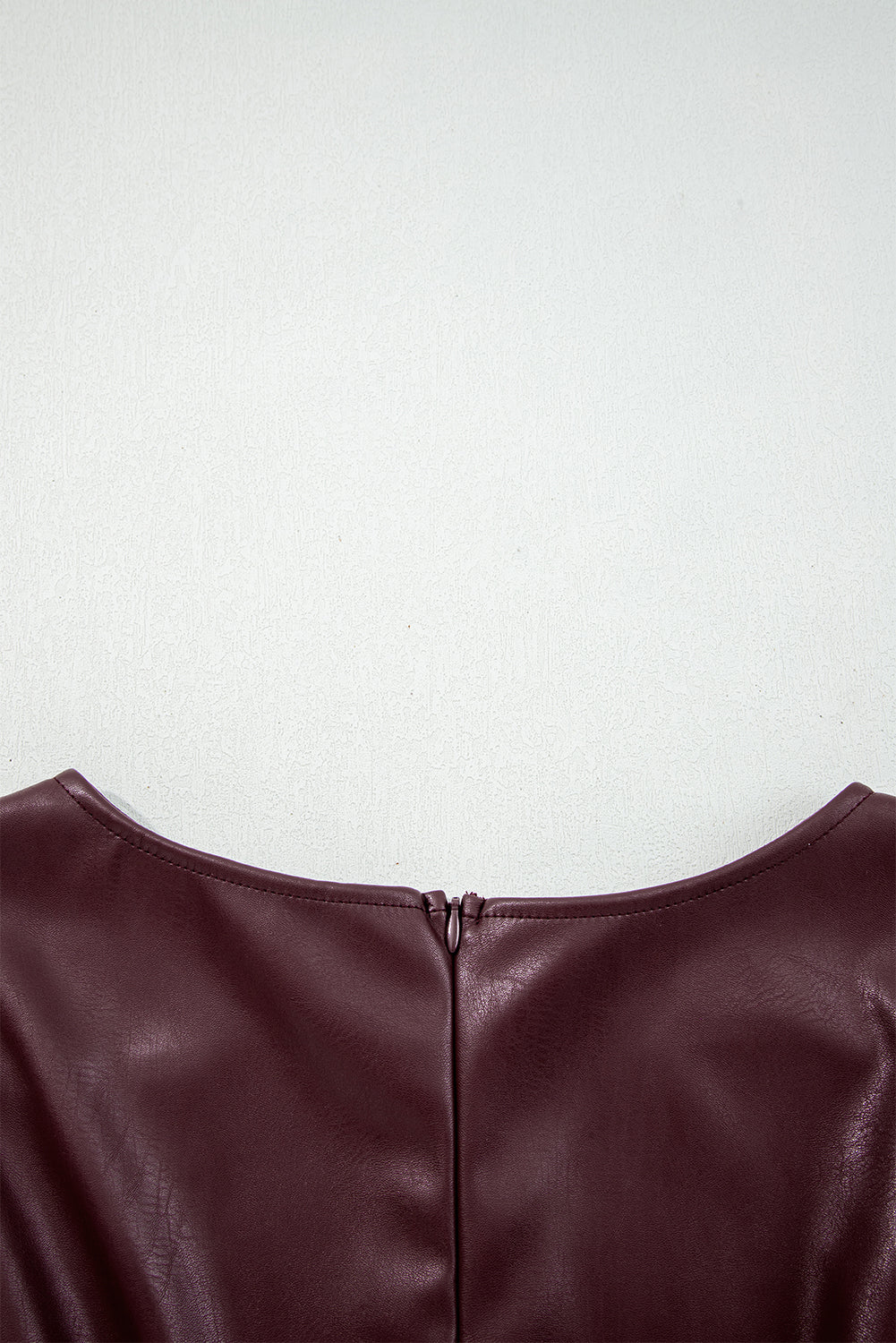 Close-up of maroon faux leather dress back with zipper detail on light background