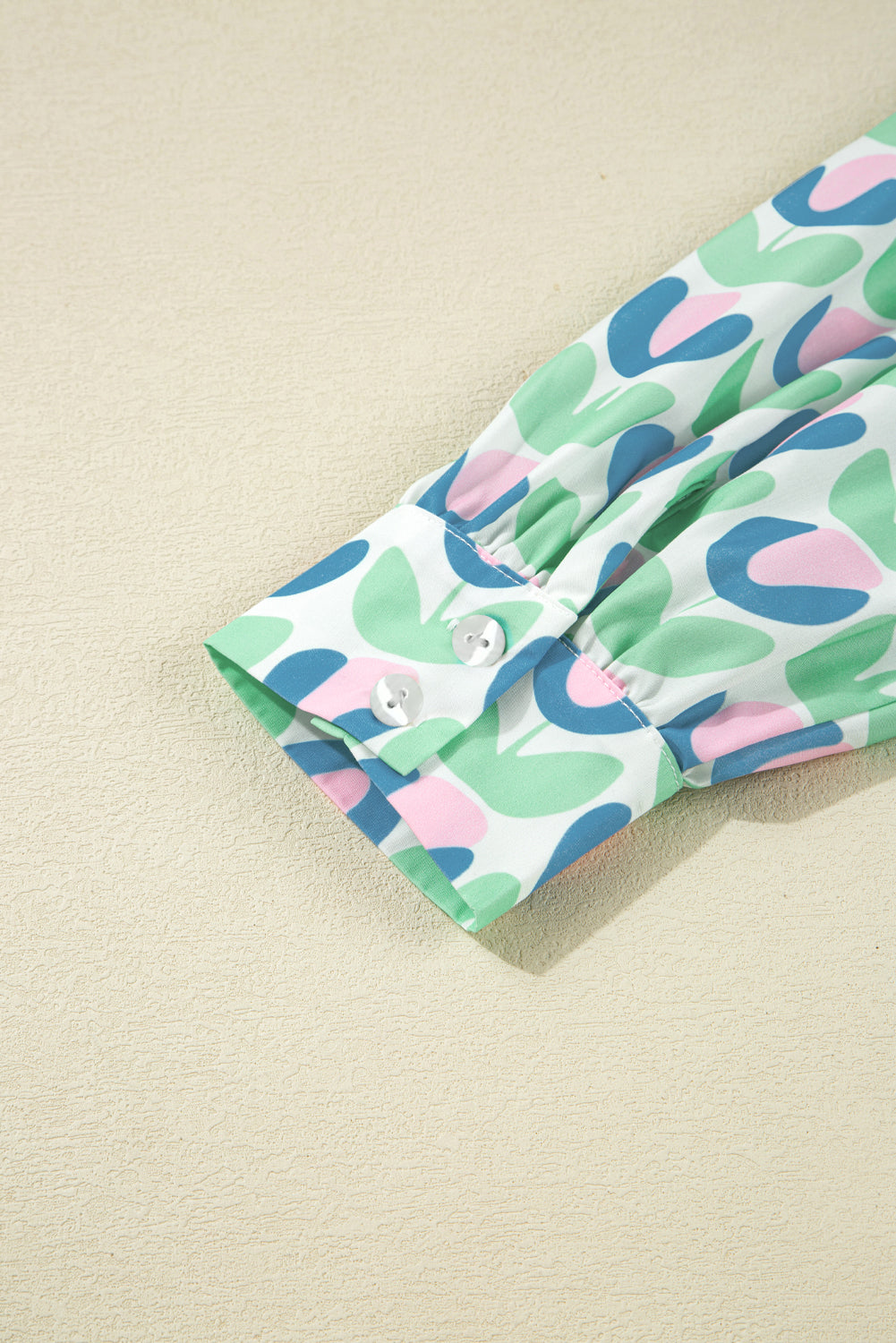 Colorful long sleeve shirt cuff with abstract green, blue, and pink pattern and white buttons