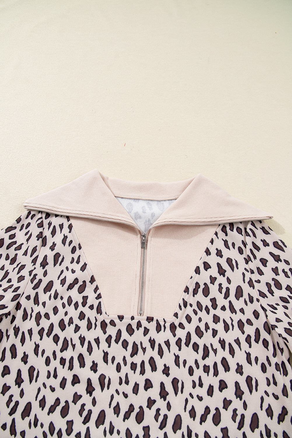 Leopard print long sleeve top with beige collar and front zipper on light background