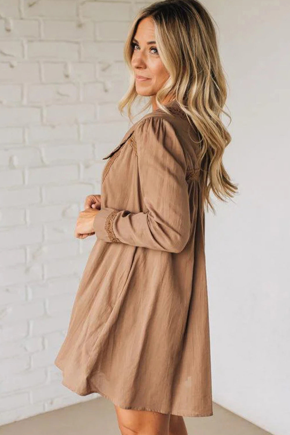 Woman in loose, long-sleeve light brown dress with textured details, white brick background