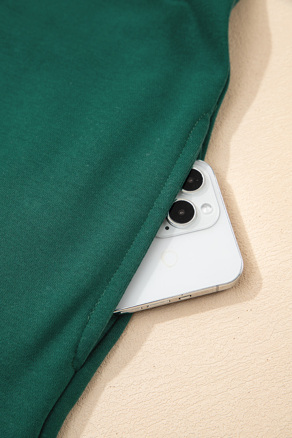 Green fabric pocket holding a white smartphone on beige textured surface
