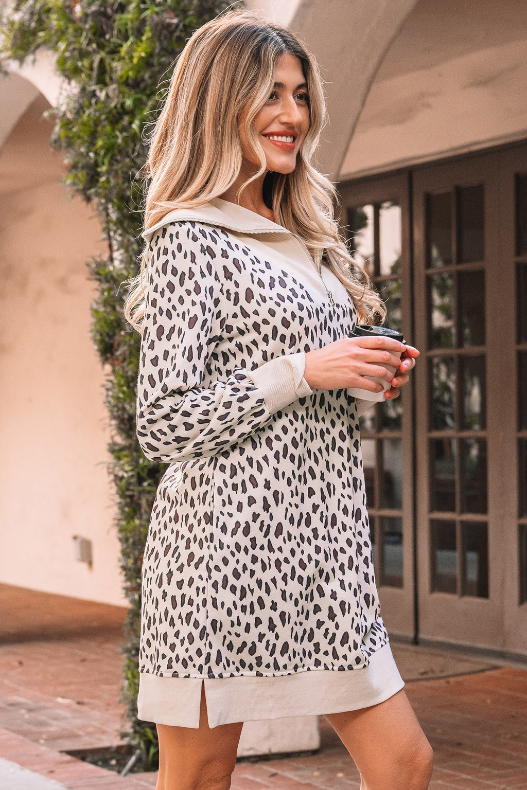 Woman wearing a long-sleeve leopard print casual dress, smiling outdoors.