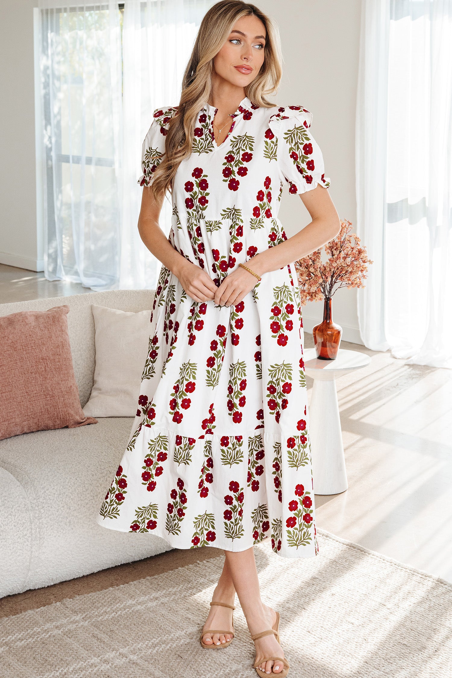 Woman wearing a white floral midi dress with red and green print, indoors, stylish summer fashion