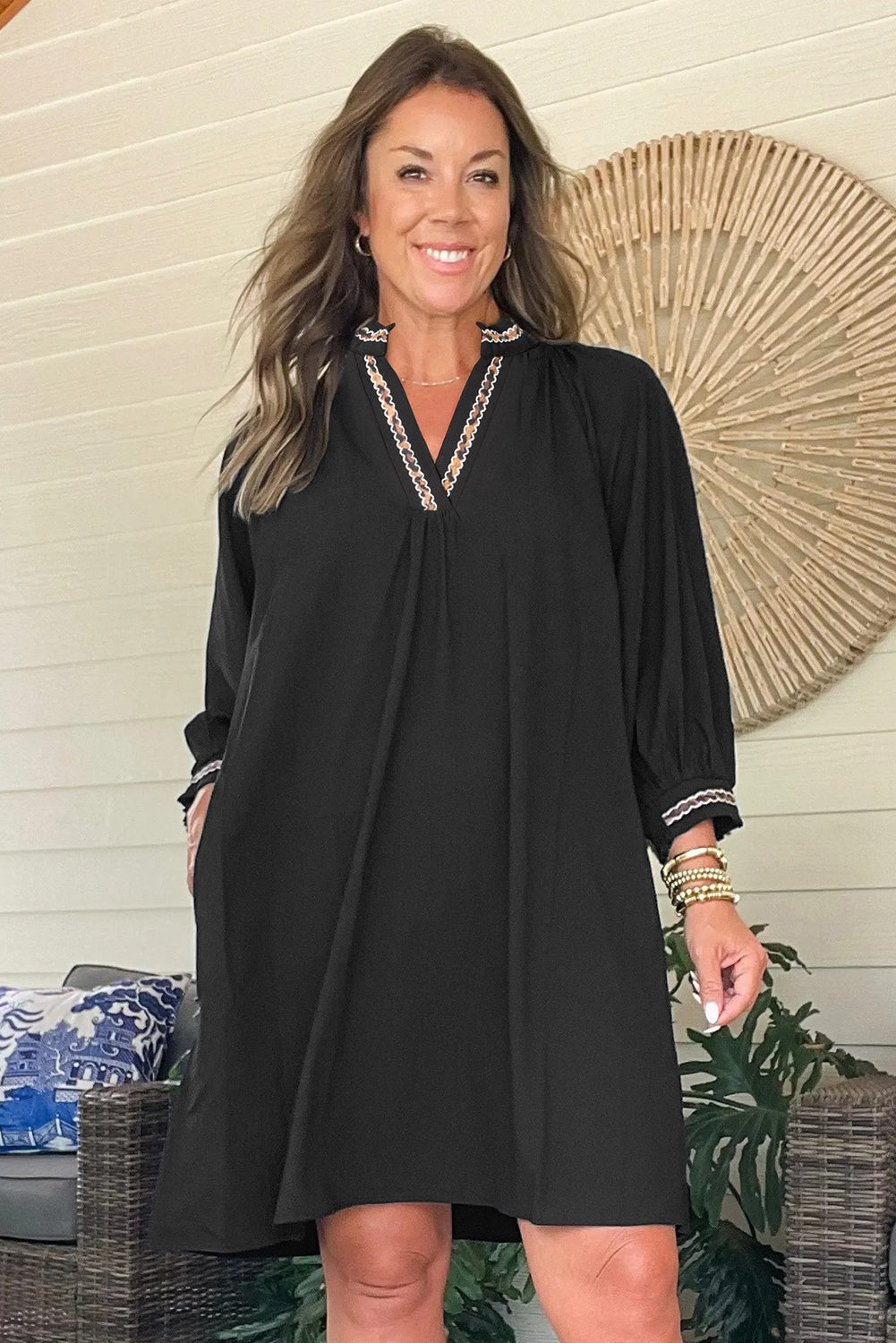 Woman wearing a loose-fit black dress with embroidered neckline and sleeves, posing indoors