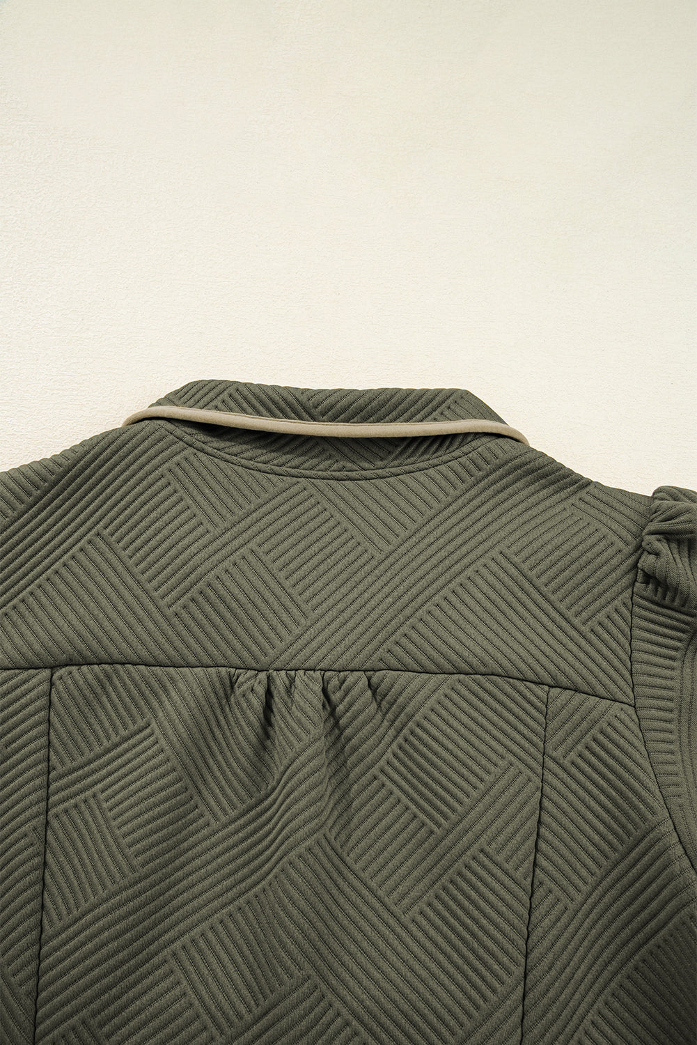 Close-up of textured olive green jacket back with geometric quilted pattern and piped collar