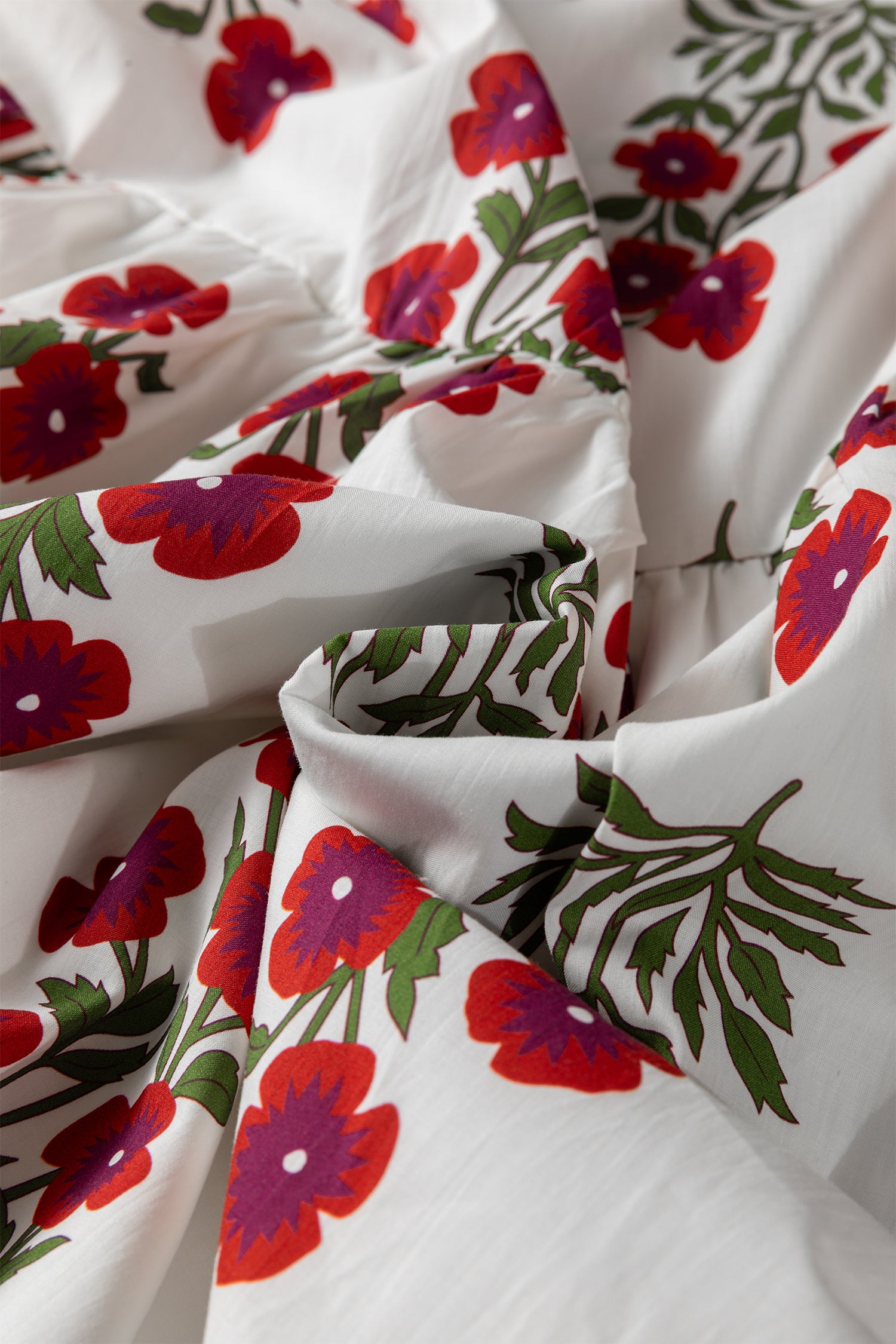 White fabric with red and purple floral print and green leaves, close-up texture