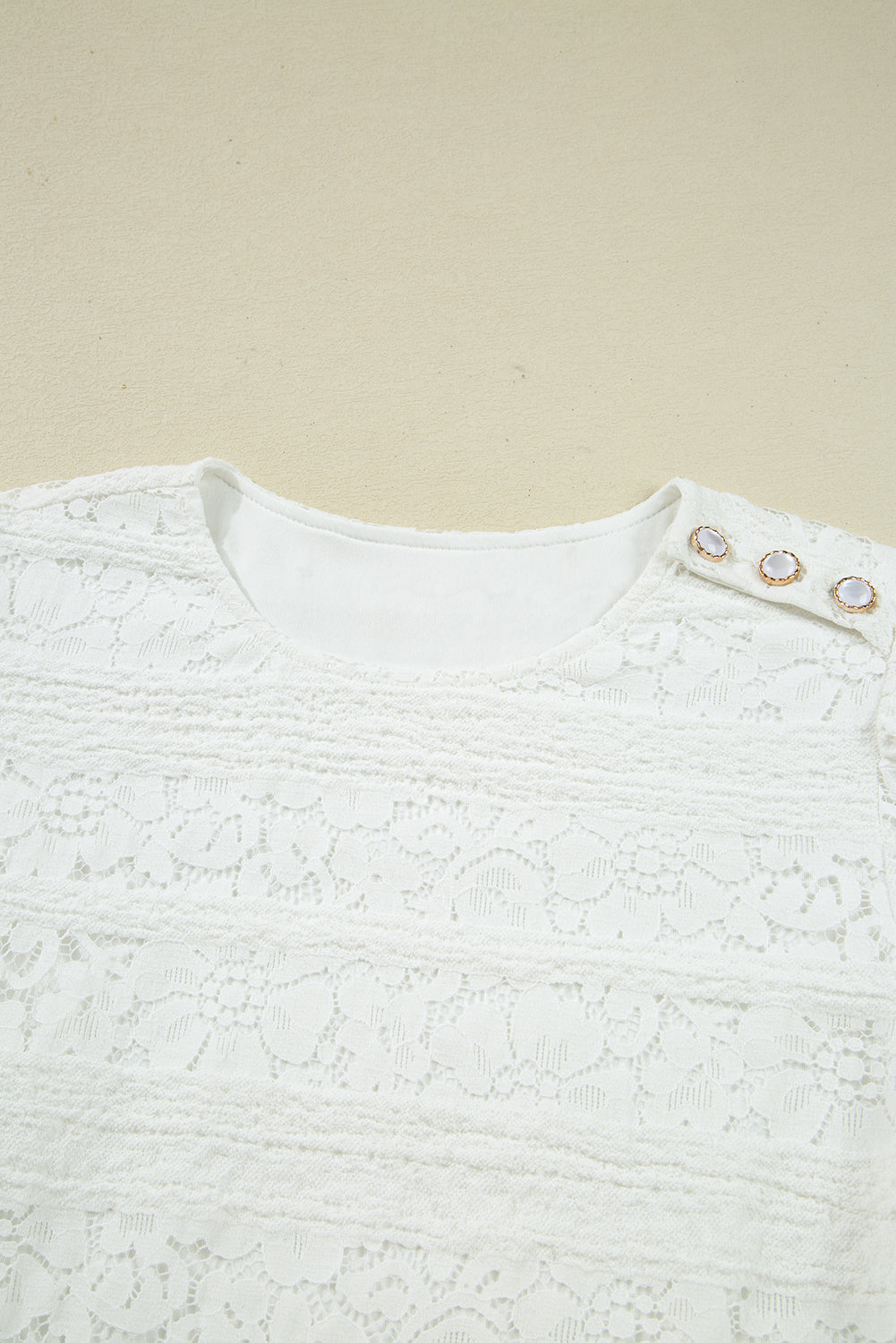 White lace blouse with round neckline and decorative buttons on the shoulder