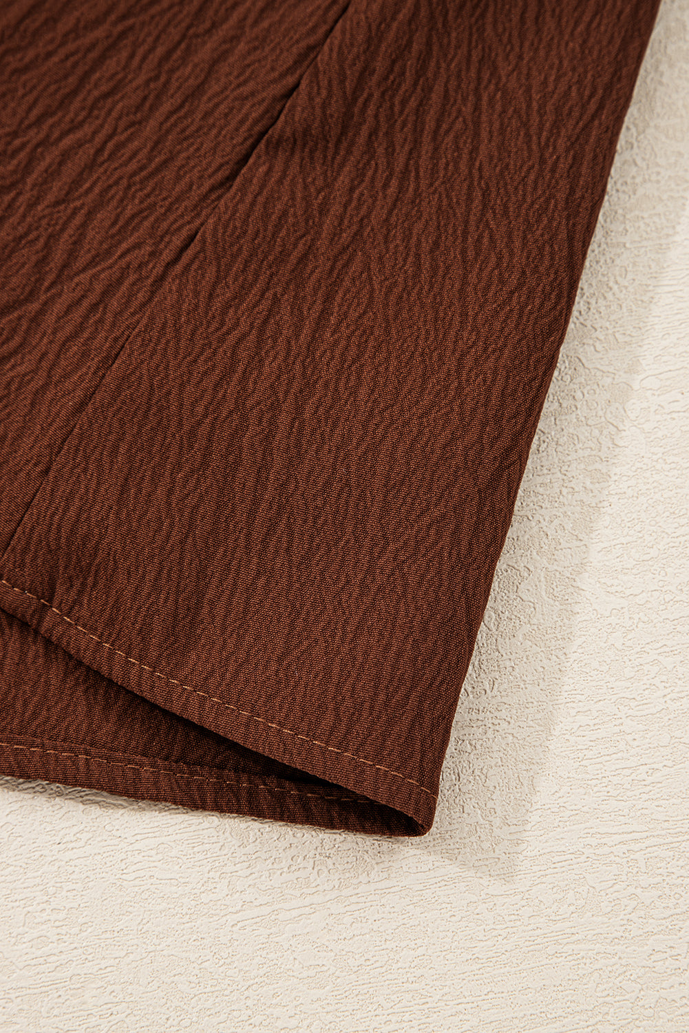 Close-up of brown textured fabric skirt hem on neutral background