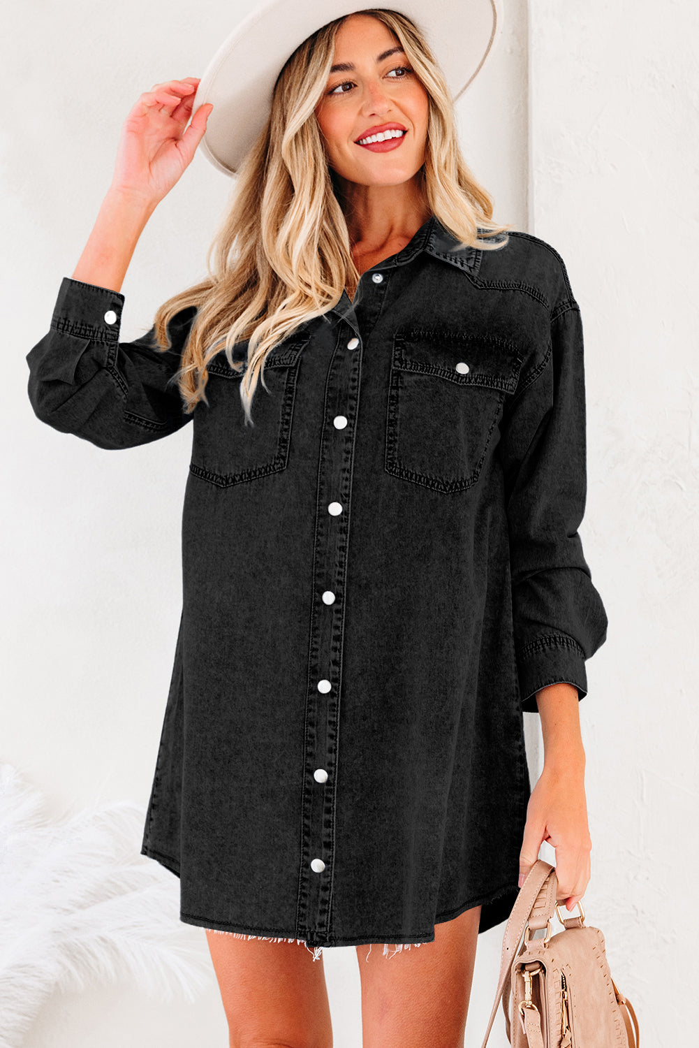 Woman in black denim shirt dress with white buttons and long sleeves, holding beige bag