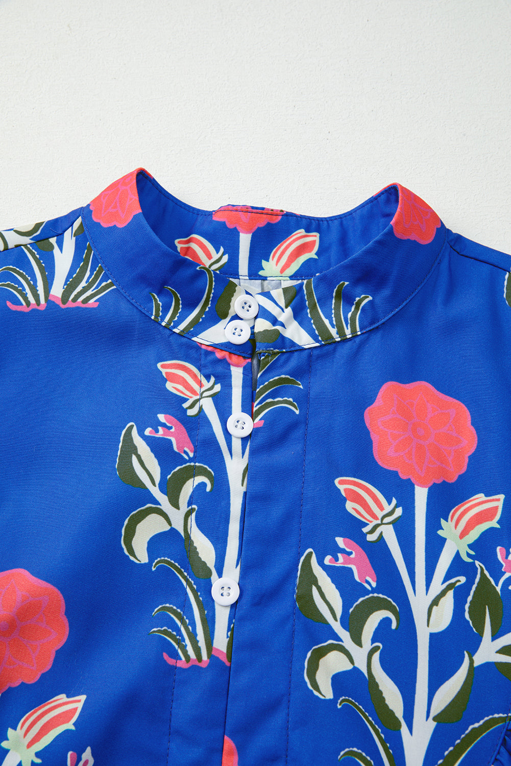 Blue blouse with colorful floral print, round collar, and white buttons