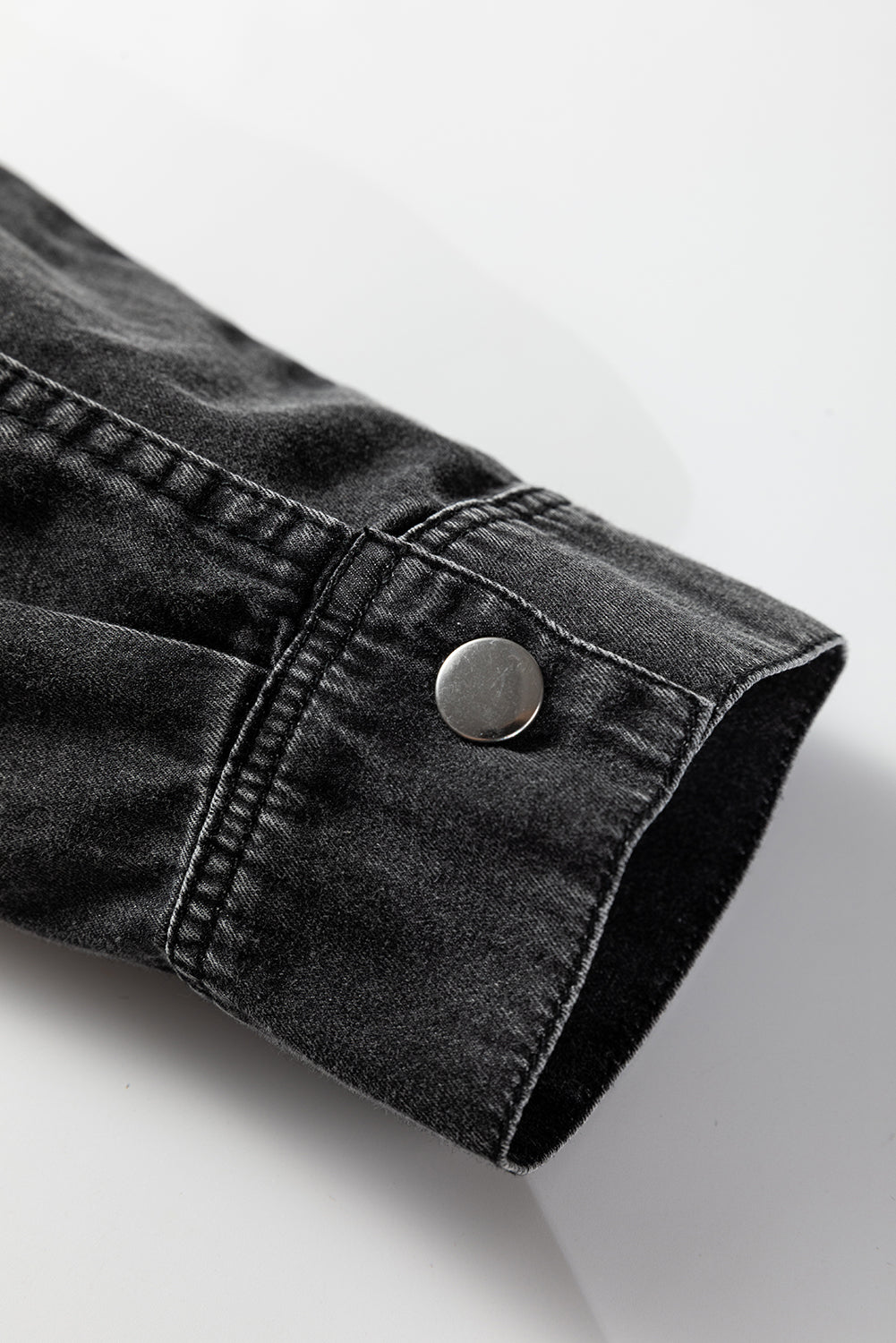 Black denim shirt sleeve with metal snap button on plain background