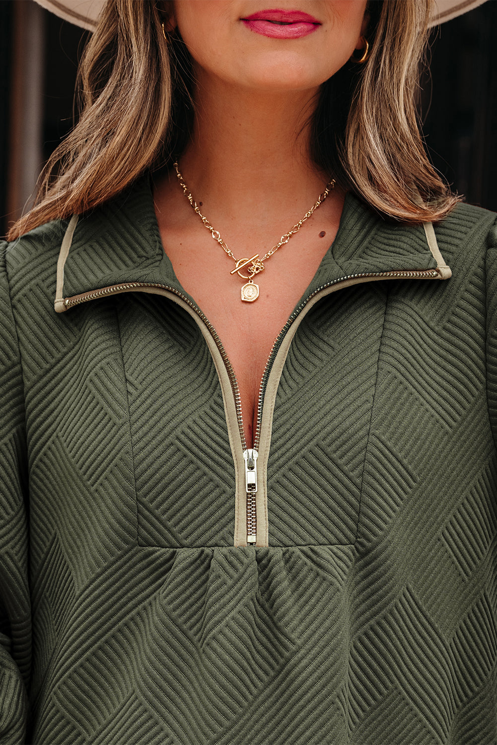 Woman in textured olive green zip-up top and gold chain necklace with pendant