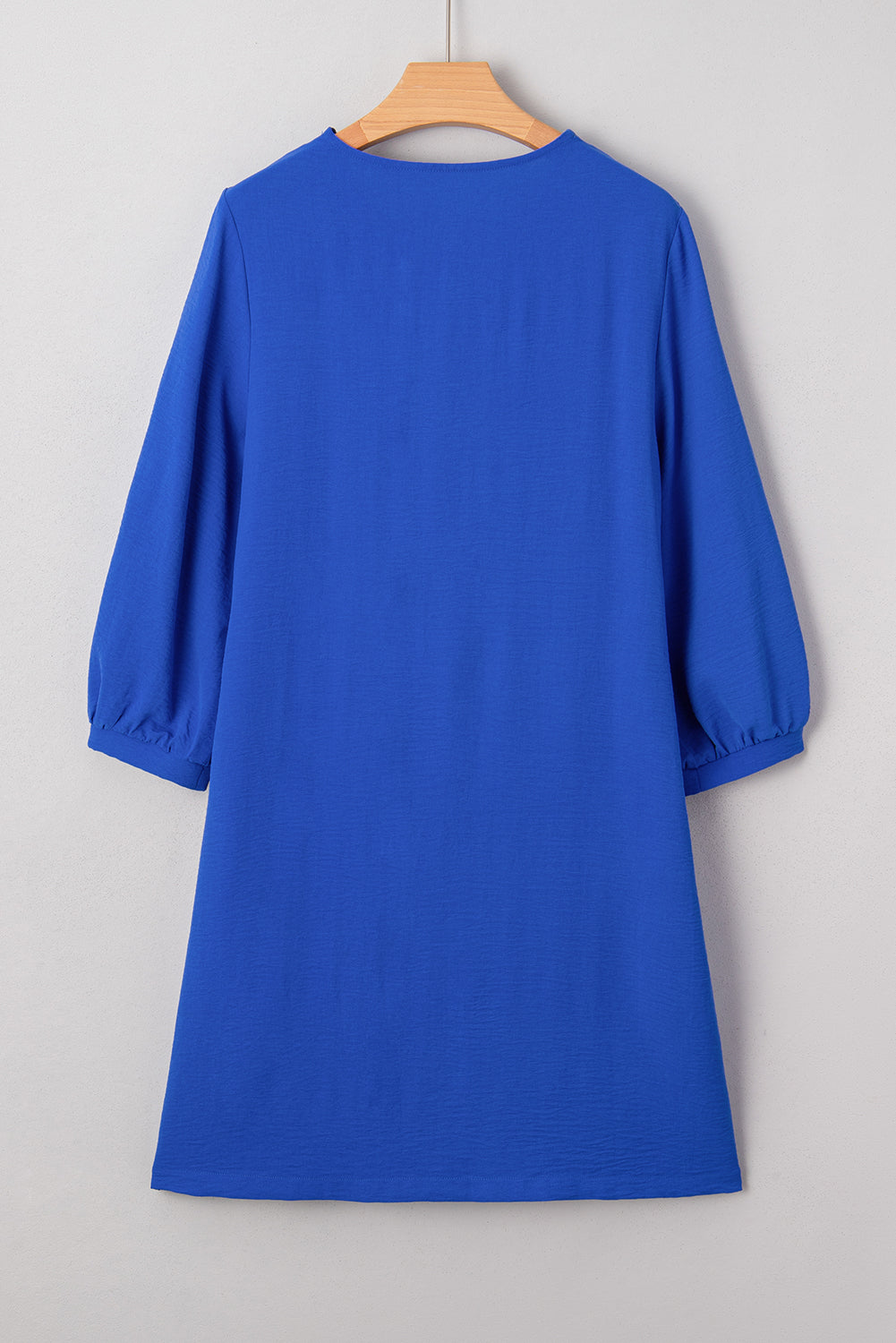 Blue knee-length dress with three-quarter sleeves on a wooden hanger, plain background