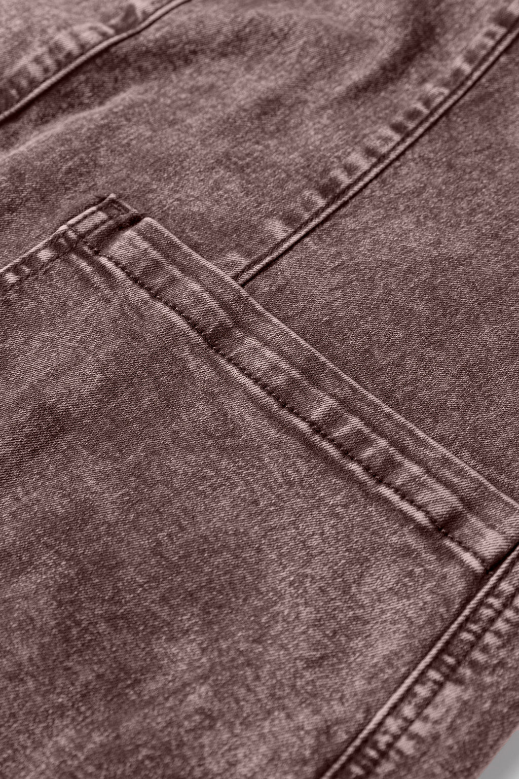 Close-up of brown denim fabric with visible seam and pocket detail, textured material