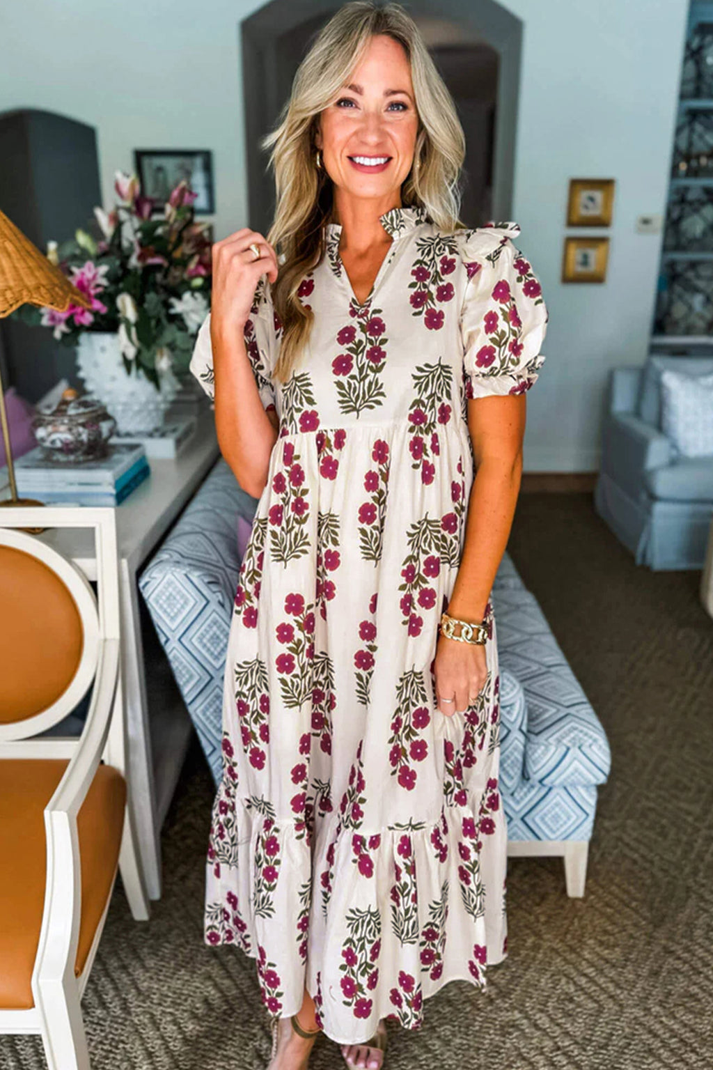 Woman in a beige floral maxi dress with puff sleeves, standing in a stylish living room