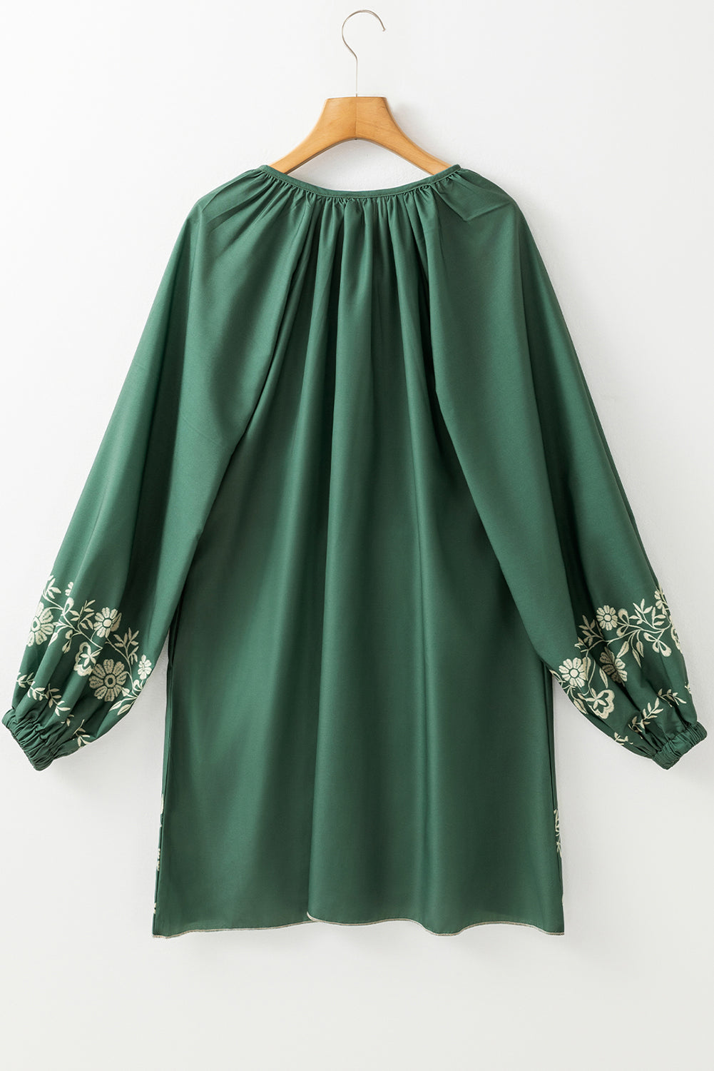 Green long sleeve tunic with cream floral embroidery on sleeves, hanging on hanger
