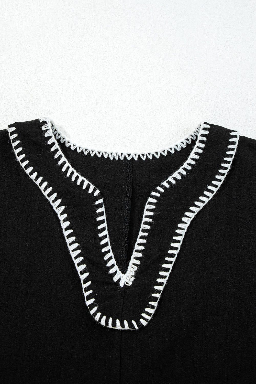 Black garment with a V-neck and white decorative stitched trim, close-up view
