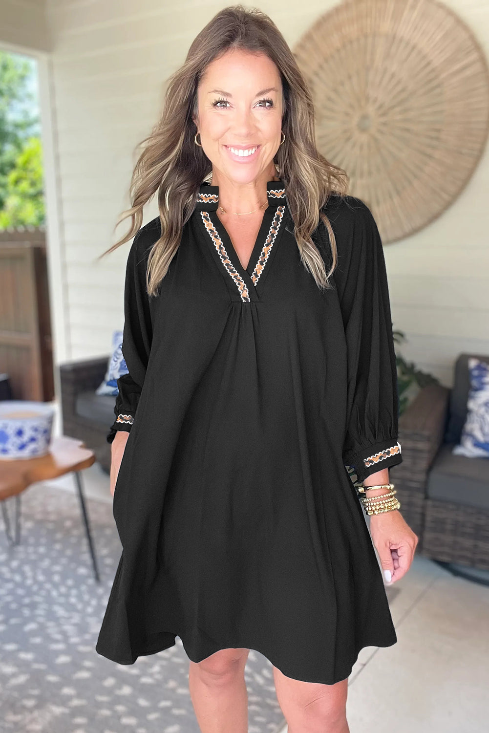 Woman wearing a black tunic dress with embroidered trim and 3/4 sleeves, smiling indoors