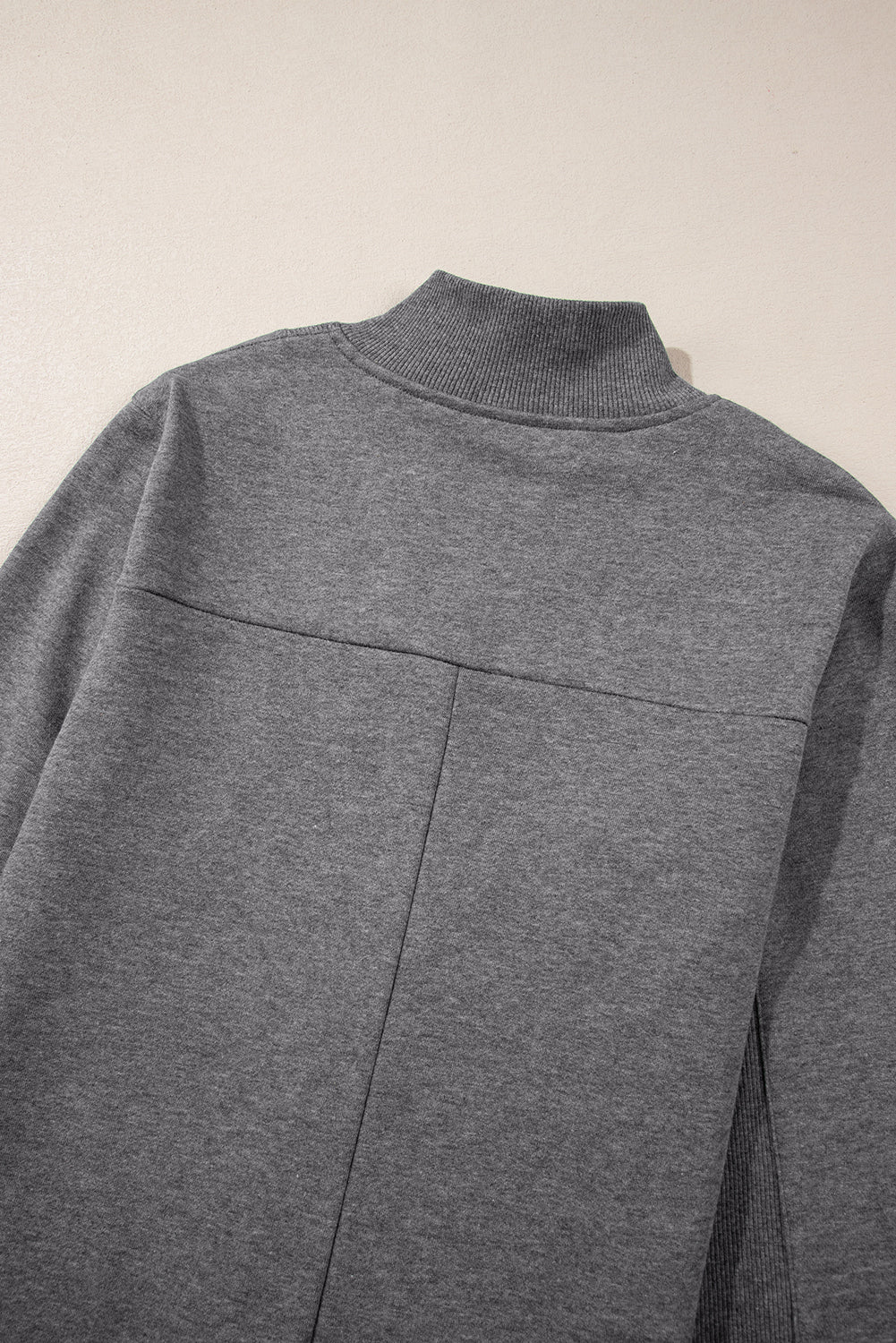 Close-up of a gray mock neck sweatshirt with ribbed collar and seam details, laid flat