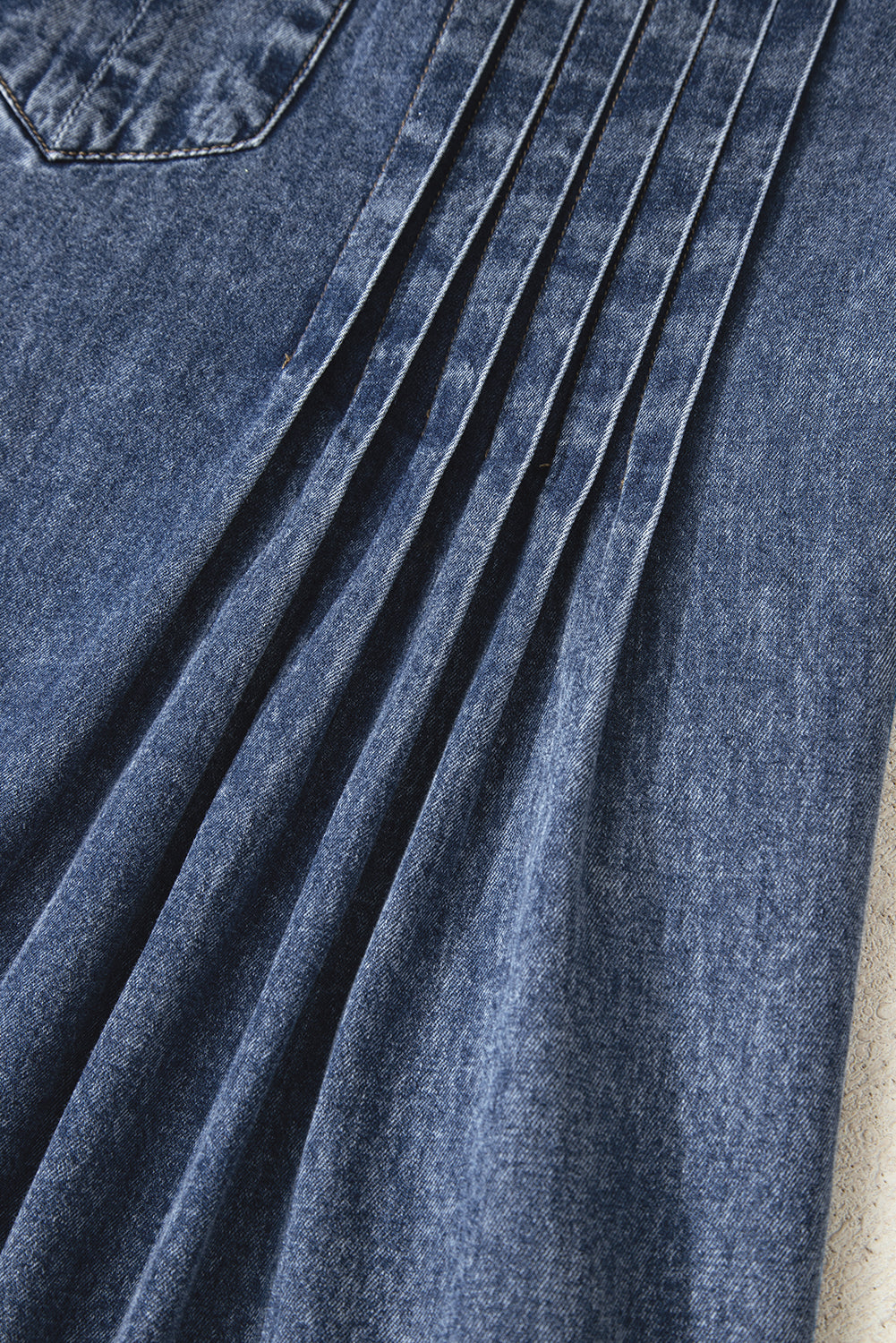 Close-up of blue denim fabric with pleated detail and a pocket