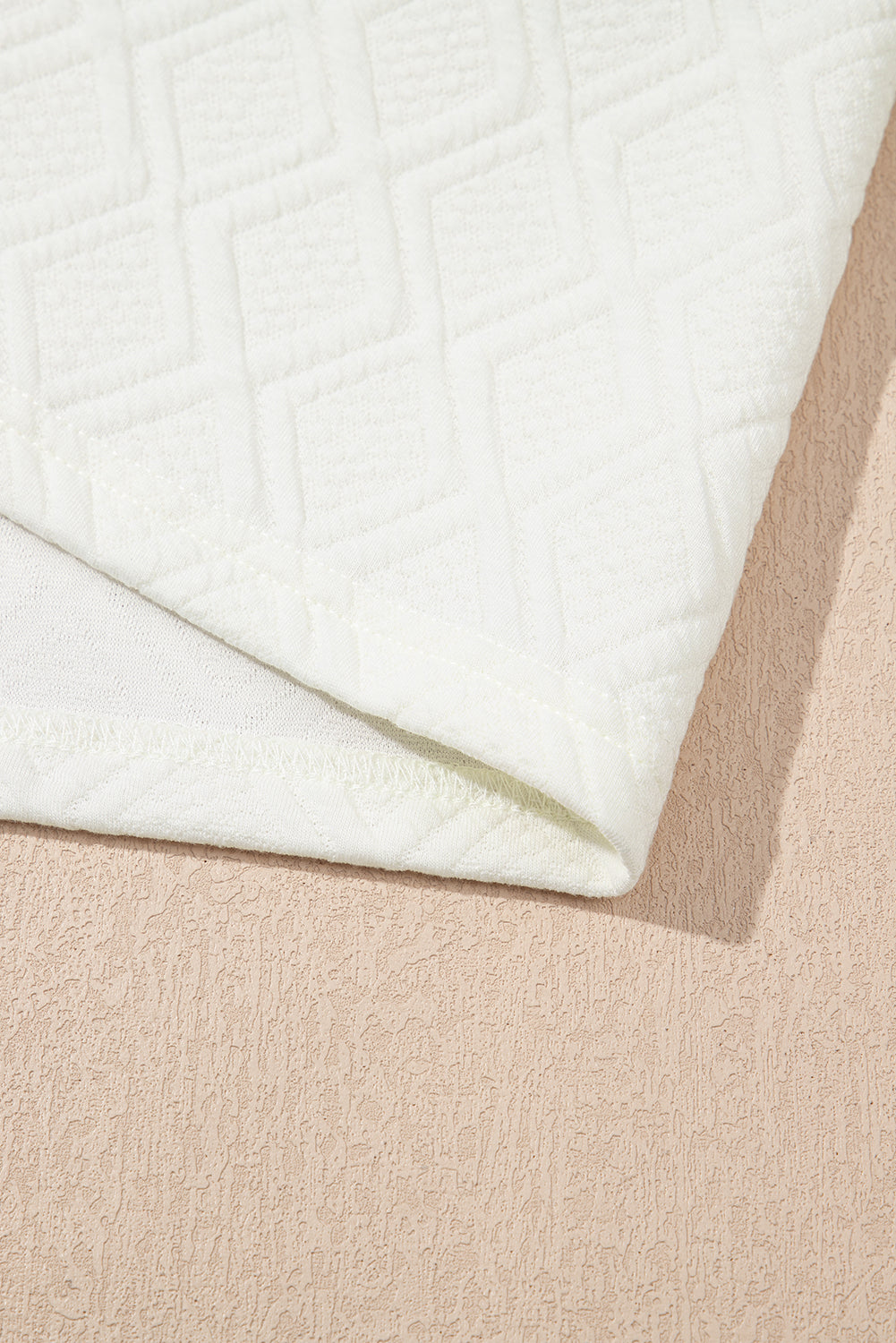 White textured fabric with geometric diamond pattern on neutral background