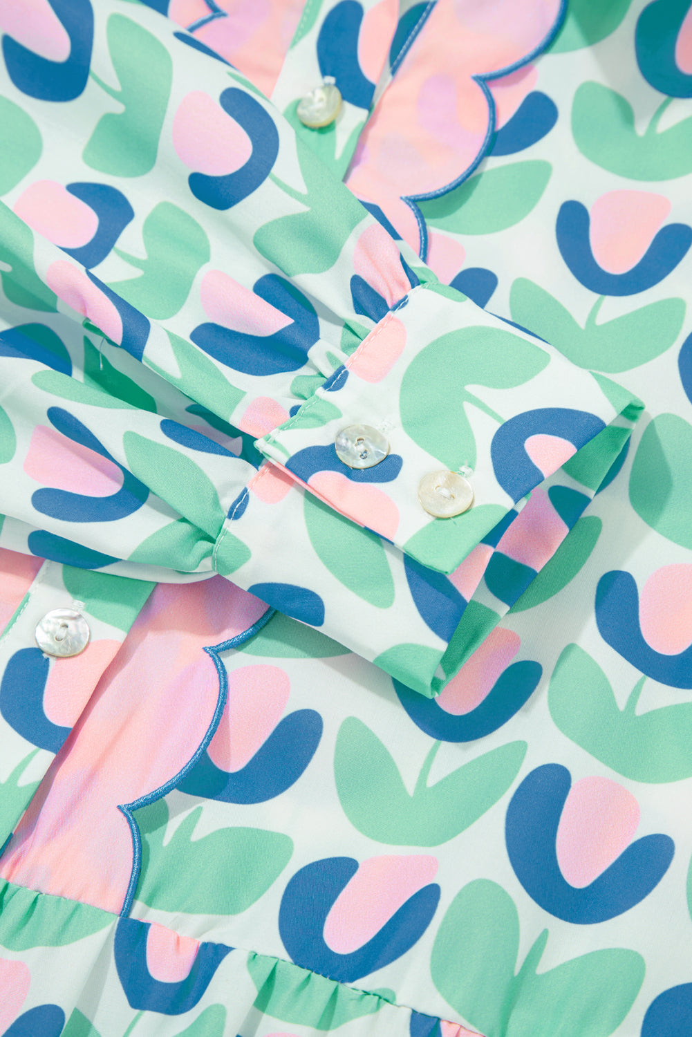 Pastel floral print blouse with scalloped trim and white buttons, close-up detail