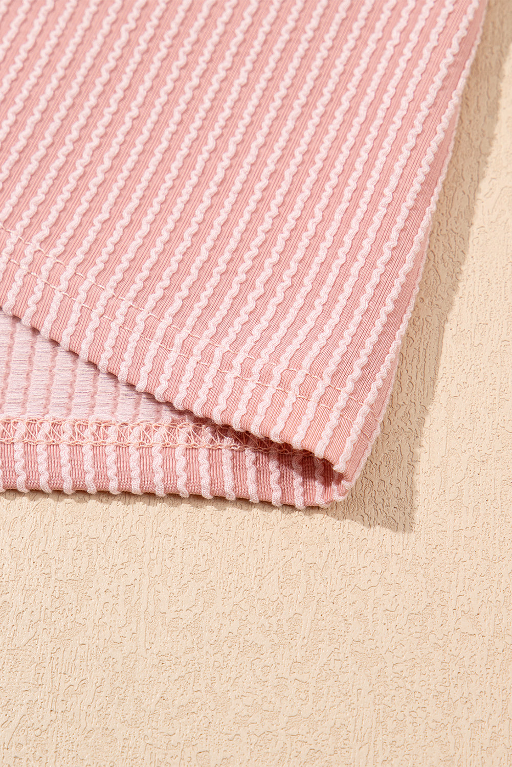 Розов рипсен текстил с вертикални релефни ленти и подгънати краища върху бежова текстурирана повърхност