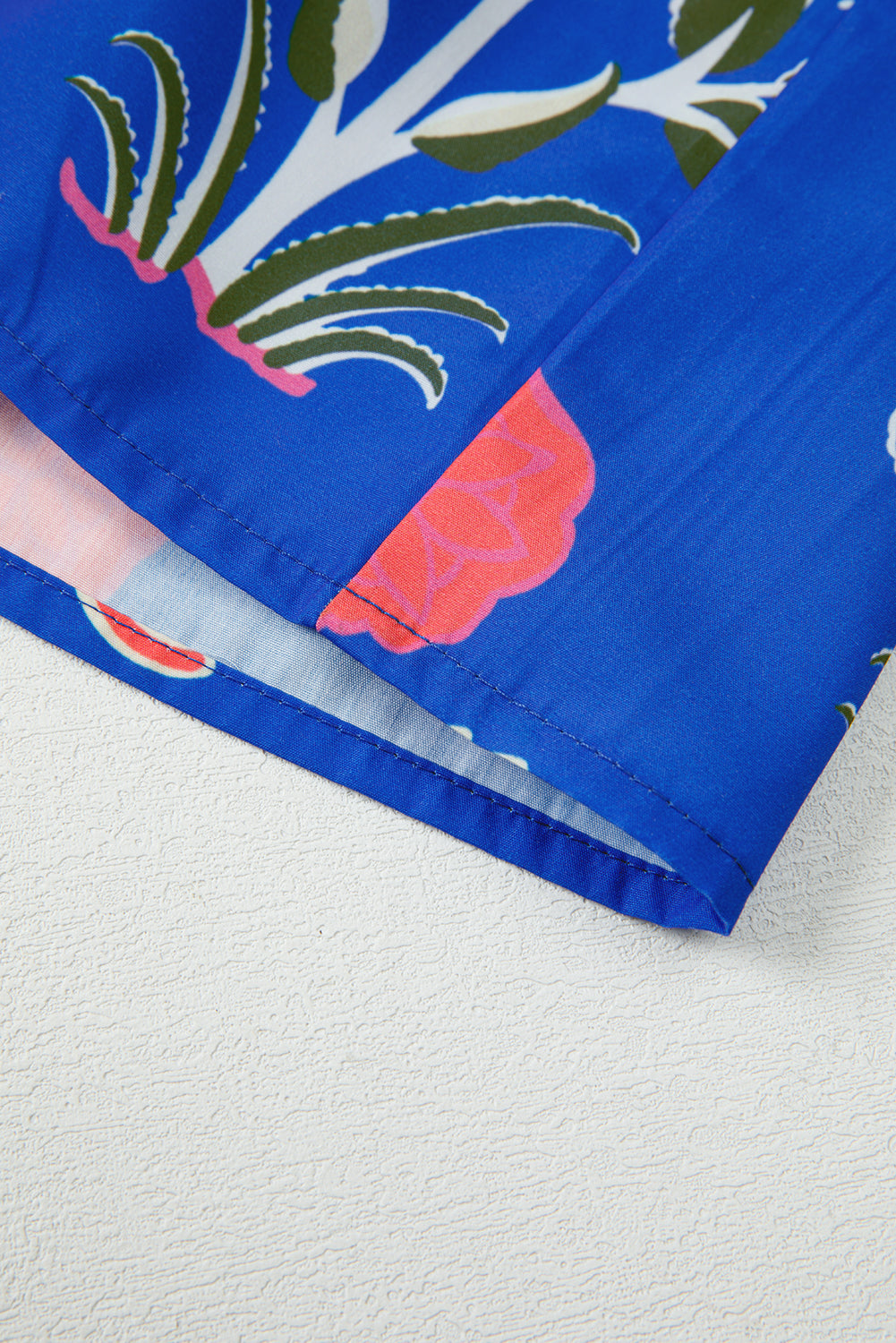 Close-up of blue floral fabric with pink and green pattern, hemmed edge detail